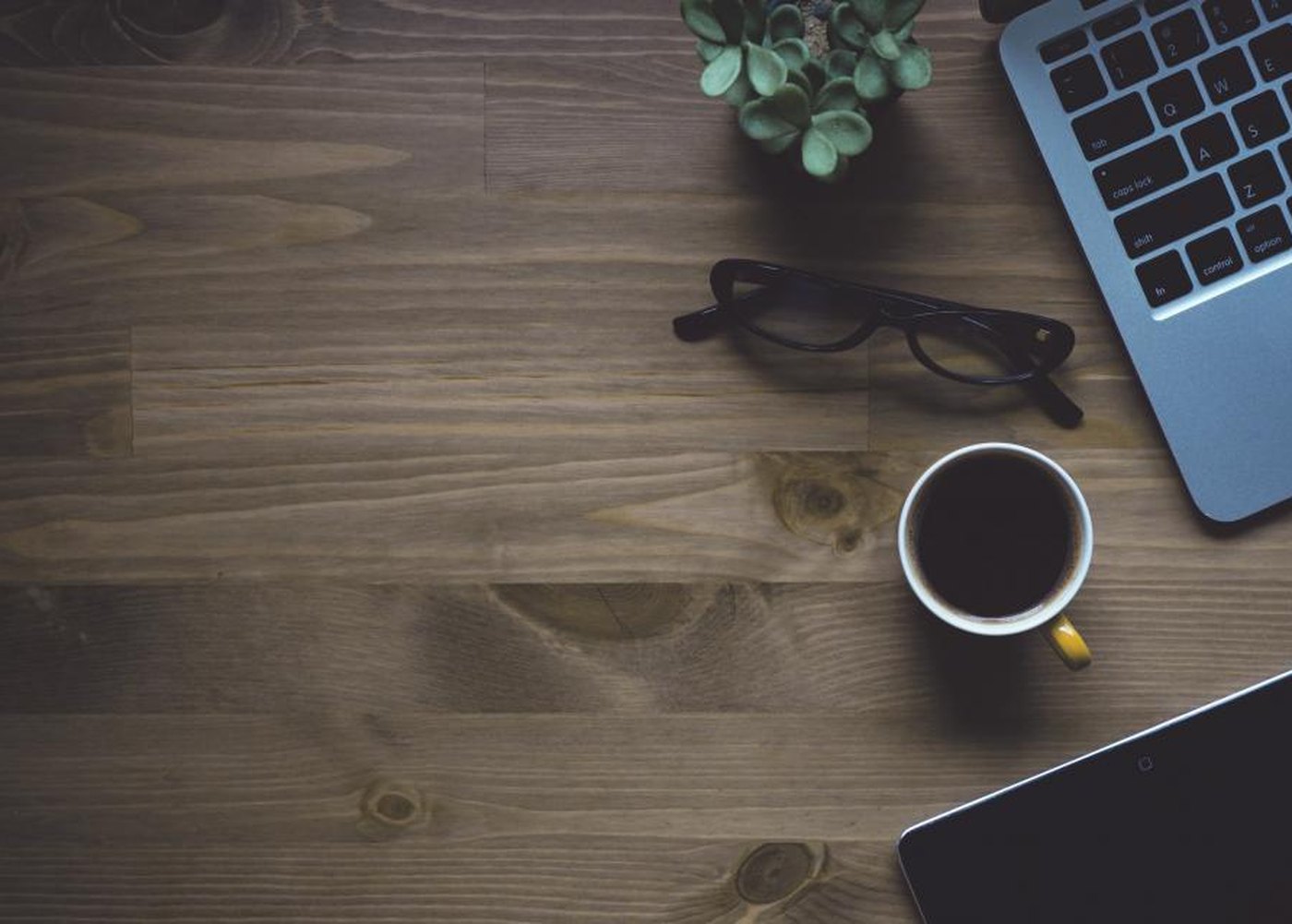 A wooden desk with a laptop, glasses and a cup of coffee