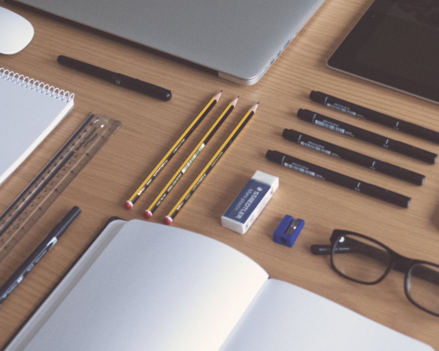 A desk laid out with a notebook, pencils, ruler and laptop